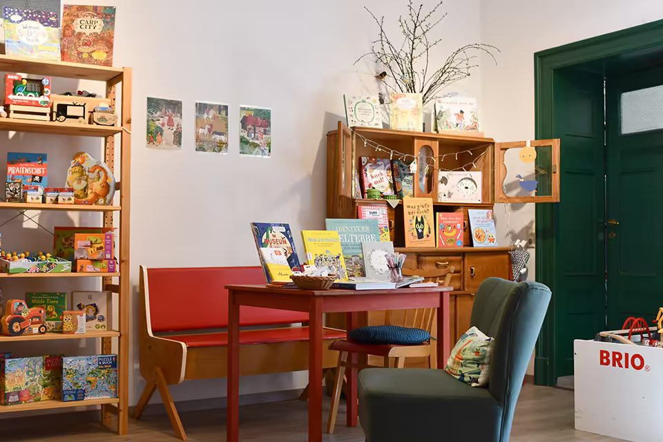 Tisch und Sessel mittig mit Bücherkommode im Hintergrund und Sachbuchregal links