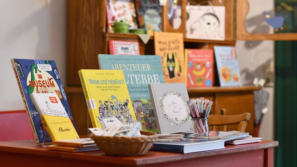 Bücher stehen auf einem Tisch, im Hintergrund ist unscharf eine Kommode mit Büchern zu sehen